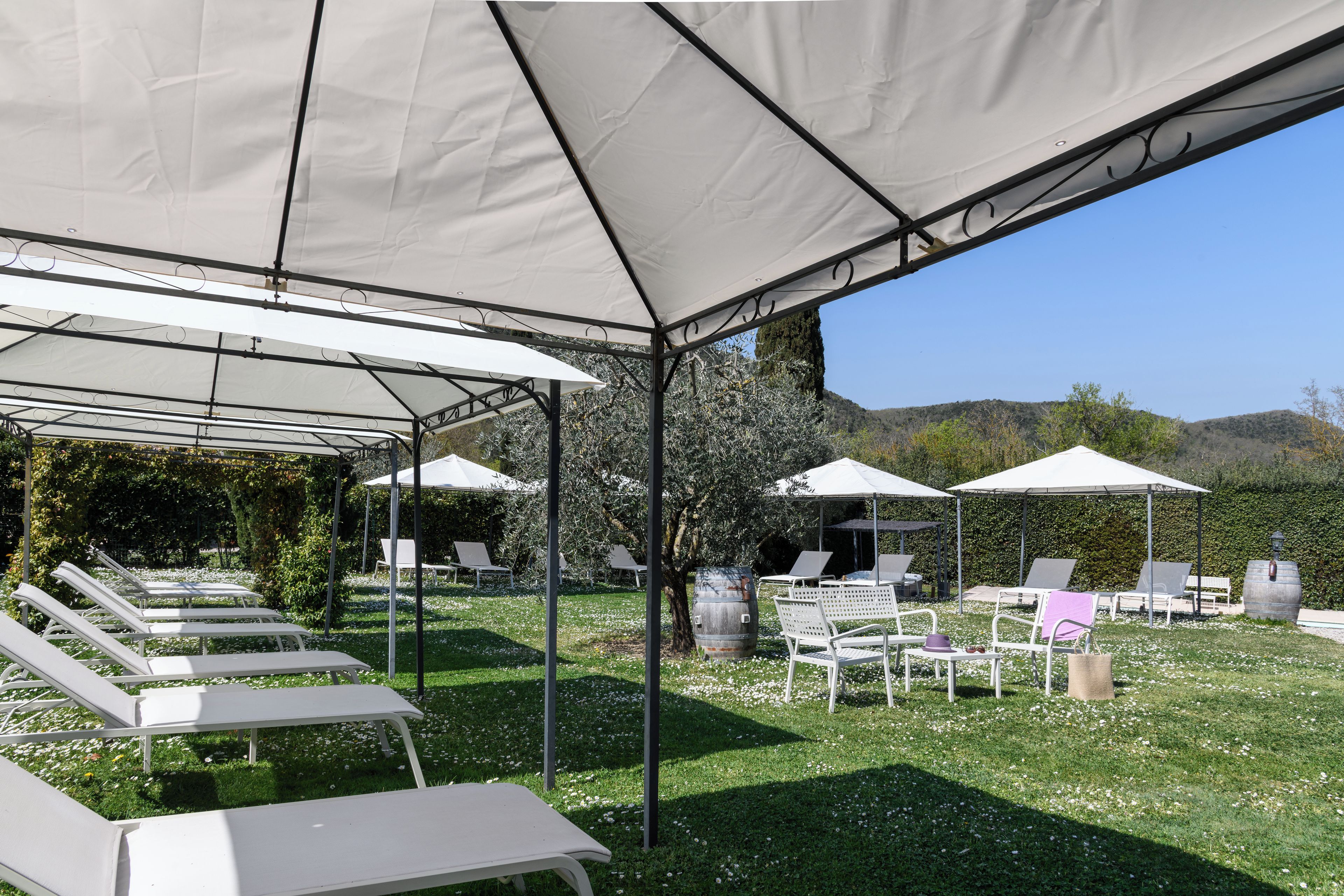 Een overdekt terras met witte stoelen en tafels, omgeven door begroeiing en heuvels op de achtergrond.