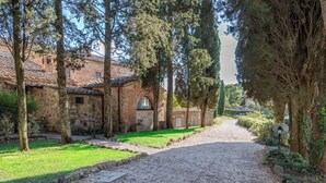A stone building with a gravel driveway, surrounded by trees and a well-maintained garden. - Abbadia Sicille Relais (Trequanda)