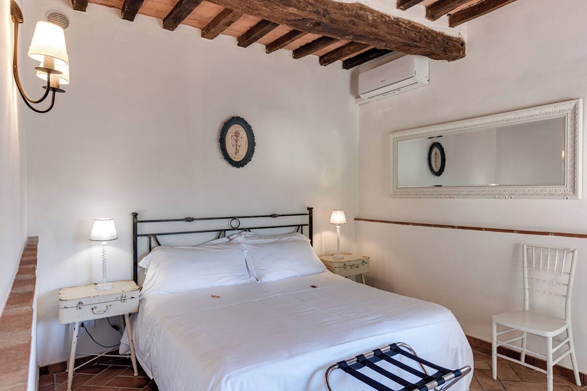 A bedroom with a bed, bedside tables, a chair, a mirror, and a wall-mounted air conditioner.
