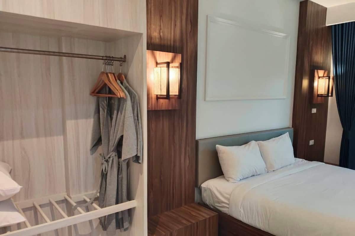 A hotel room with a wooden headboard, a bed with white linens, a hanging robe, and a wooden wardrobe.