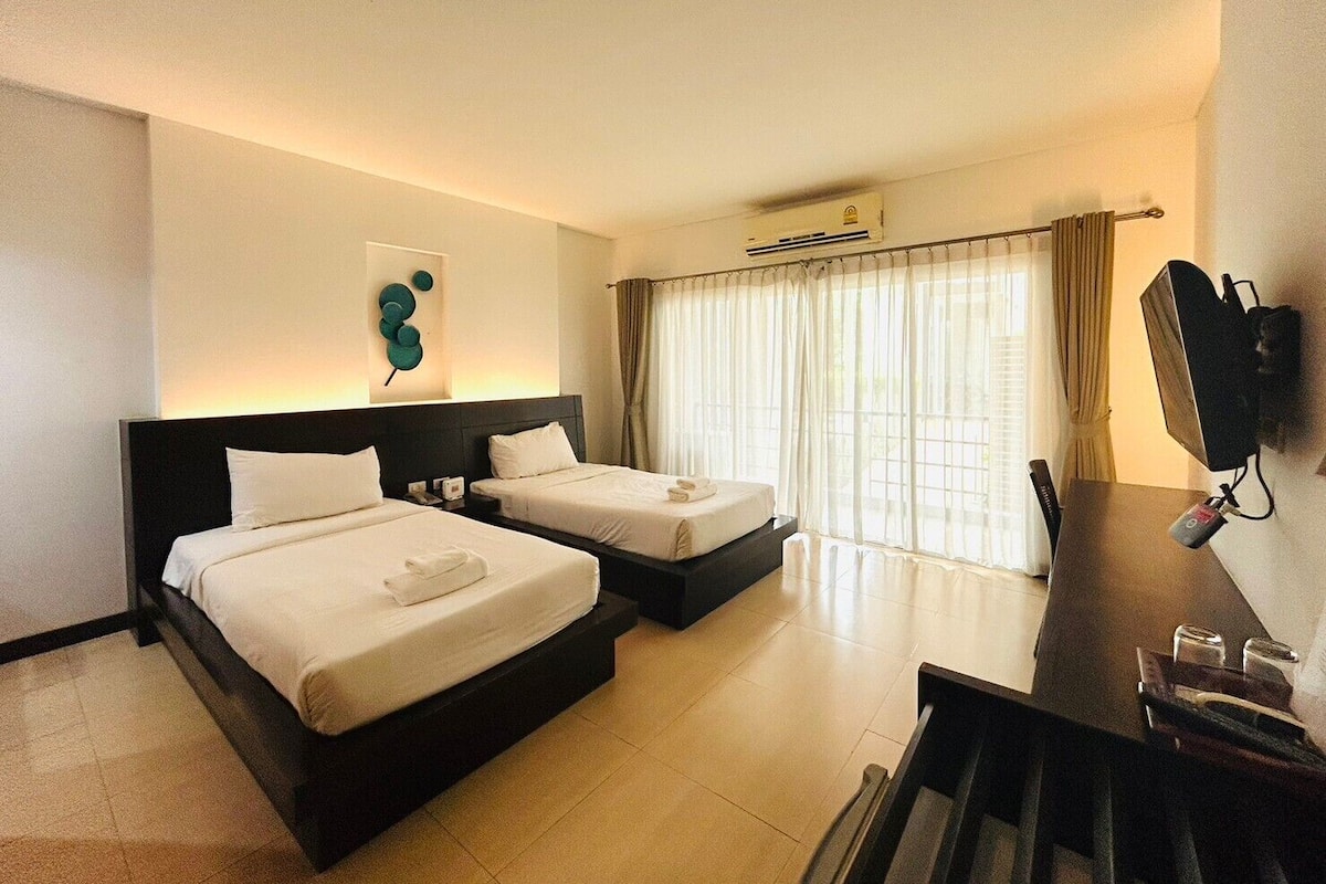 A hotel room with two beds, a desk, a TV, and a window with curtains.