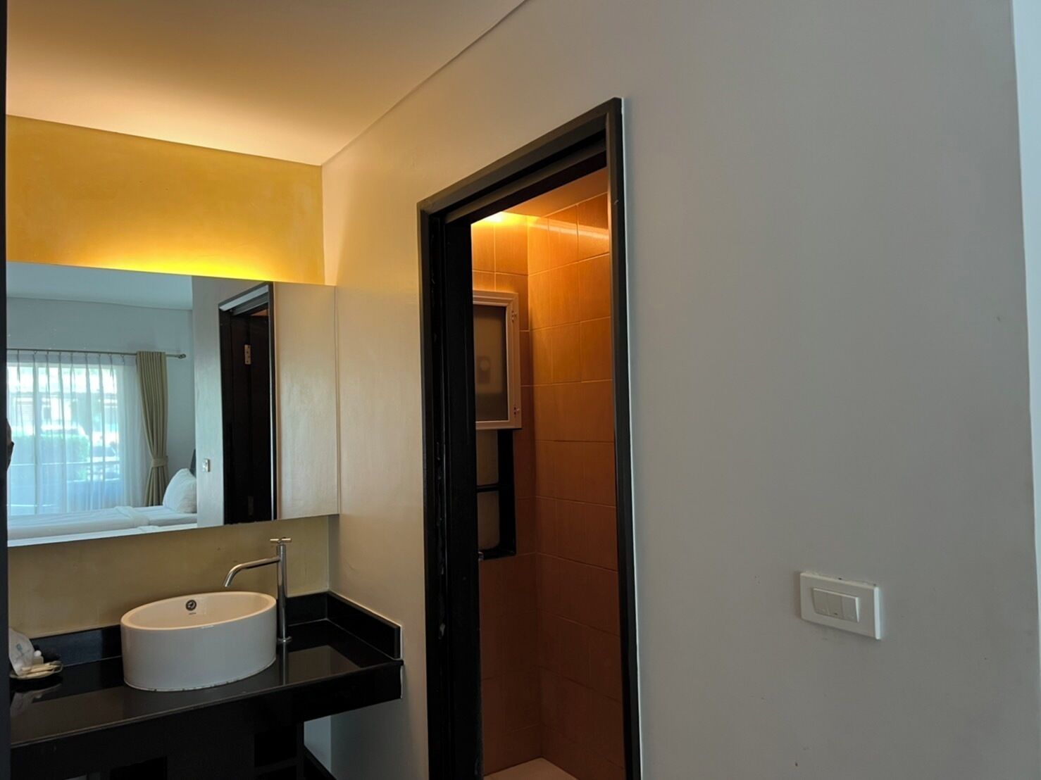 A modern bathroom with a white sink, a mirror, and a shower area visible through an open door.