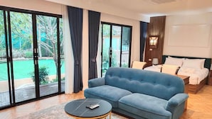 Una habitación de hotel moderna con un sofá azul, una mesita de centro redonda y una cama con ropa de cama blanca.