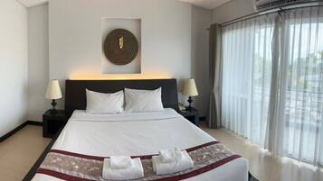 Una habitación de hotel con una cama grande, dos mesitas de noche con lámparas, una obra de arte colgada en la pared y vistas a través de cortinas de gasa.