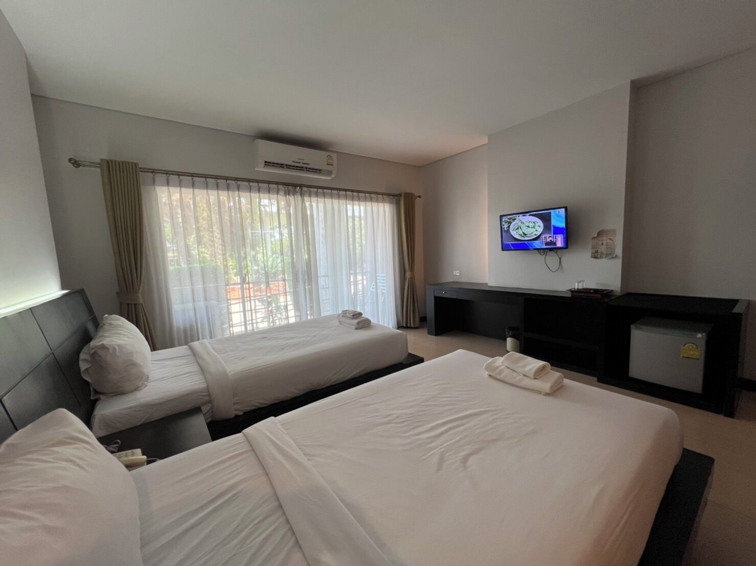 Ein Hotelzimmer mit zwei Betten, einem Flachbildfernseher, einem Schreibtisch und einer Klimaanlage.