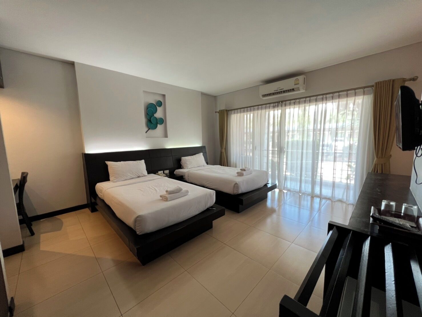 A hotel room with two beds, a desk, and a TV.