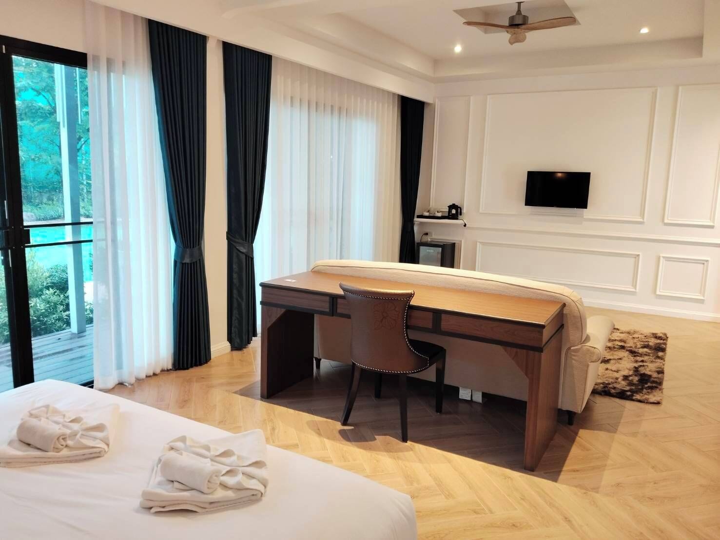 A hotel room with a bed, a desk, a chair, a TV, and a view of the outdoors.