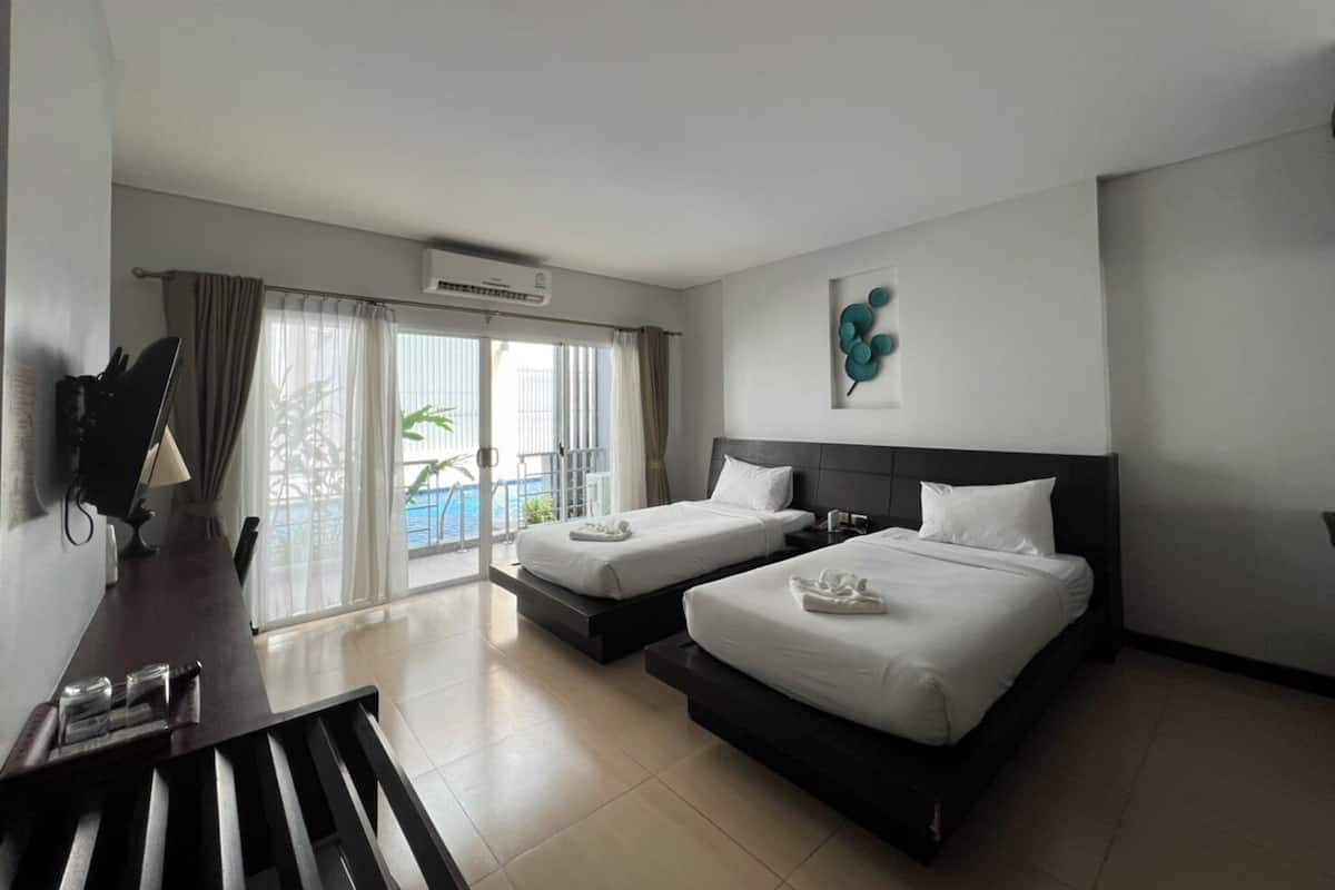 A hotel room with two beds, a desk, and a view of the sea through large windows.