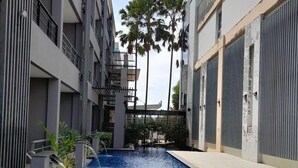 Una piscina con una escalera metálica, rodeada de edificios modernos con balcones y una palmera al fondo.