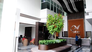 Un moderno vestíbulo de hotel con una mesa de recepción, una planta de interior grande y una escalera que conduce a los pisos superiores.