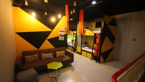 A modern interior with a sofa, ottoman, and geometric wall design. - The Hive Hatyai Hostel (Hat Yai)