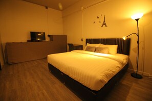 A neatly made bed with a headboard, a bedside table, a lamp, and a television on a stand. - The Hive Hatyai Hostel (Hat Yai)
