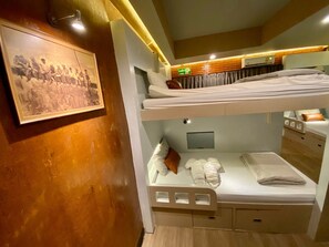 A bunk bed room with a framed picture on the wall, a fire exit sign, and a small window. - The Hive Hatyai Hostel (Hat Yai)