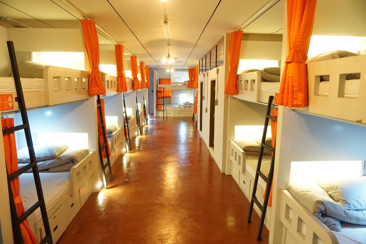 A corridor with bunk beds, orange curtains, and a central light fixture.