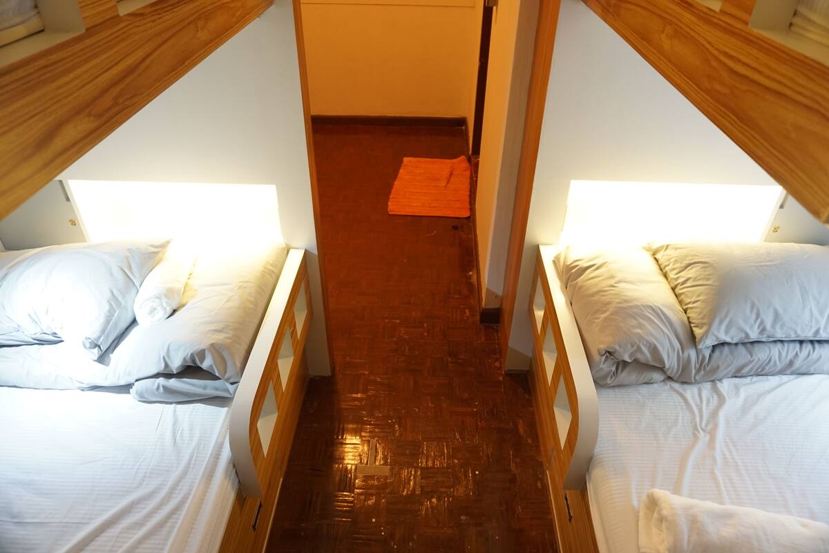 A room with two beds, wooden bunk beds, a wooden floor, and a small orange rug.