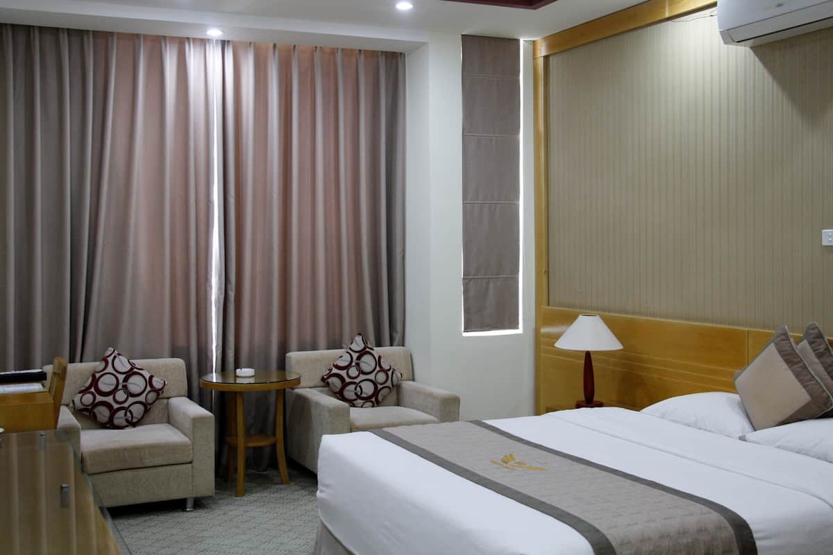 A hotel room with a bed, a chair, a small table, and curtains.