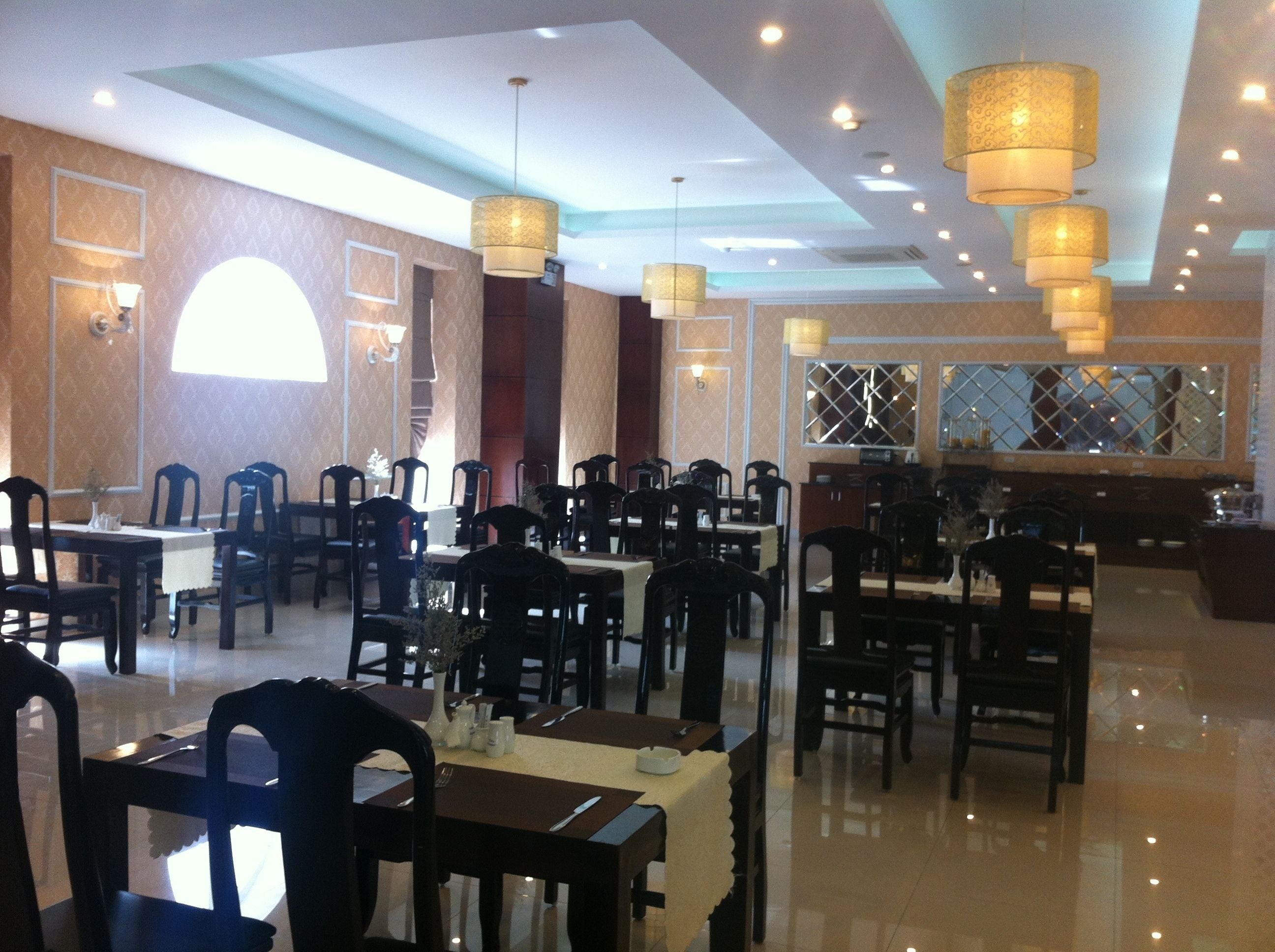 A restaurant with multiple tables and chairs, ceiling lights, and a large window with a view.