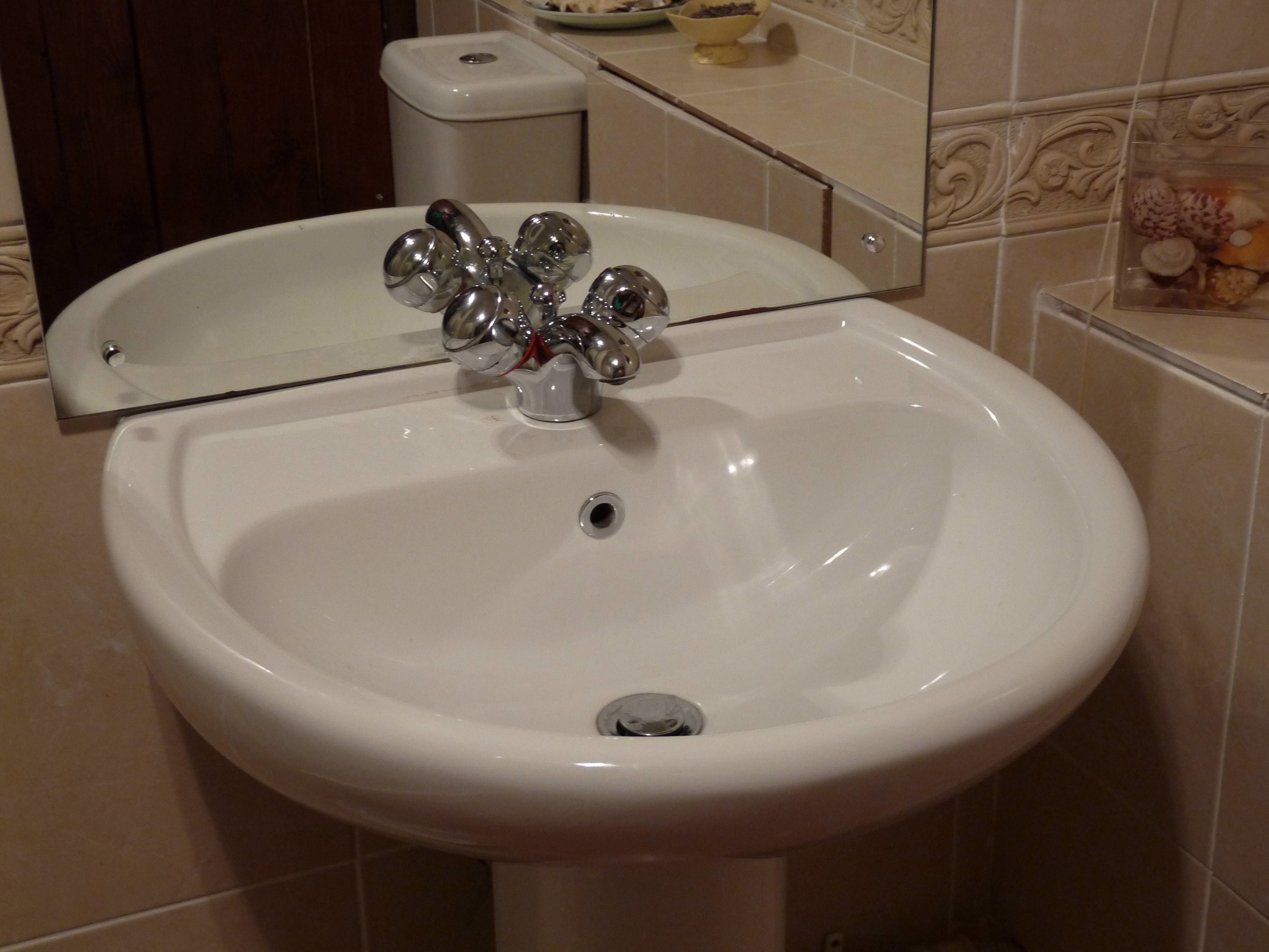 A white bathroom sink with a mirror above it, a toilet in the background, and a tiled wall with a decorative border.