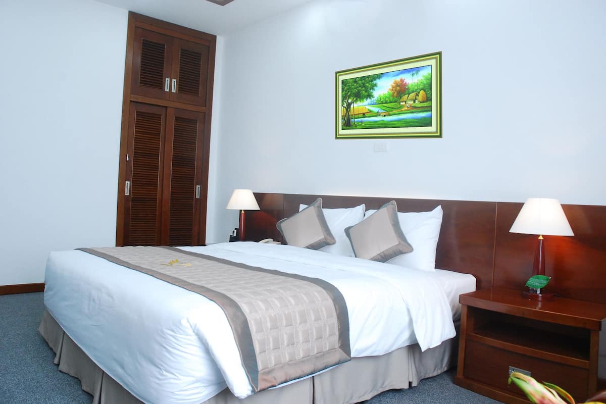 A neatly made bed with a headboard, two bedside lamps, and a nightstand with a vase.