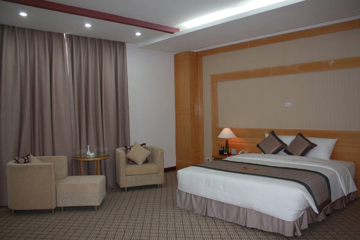 A hotel room with a large bed, two armchairs, a small table, and a lamp.