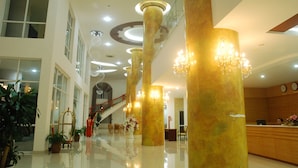 Un vestíbulo amplio con techos altos, grandes columnas doradas y una escalera que conduce a un piso superior.