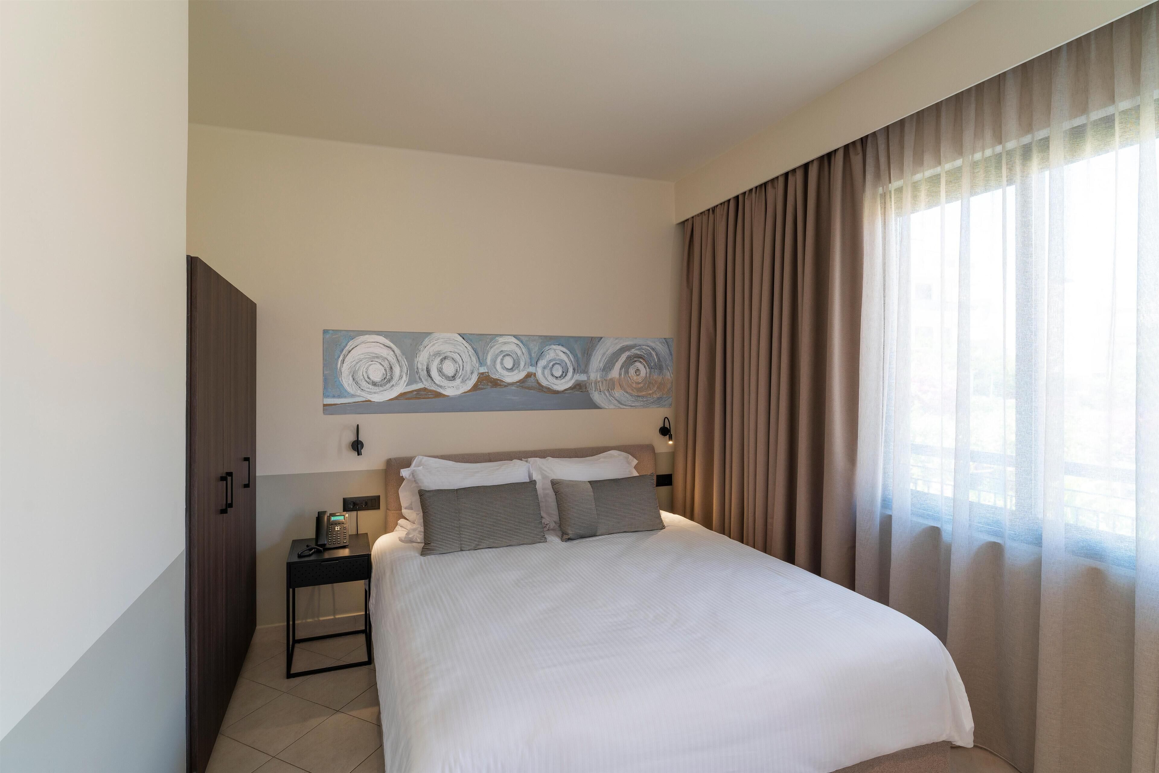 Een hotelkamer met een groot bed, een nachtkastje met een telefoon en een schilderij aan de muur.