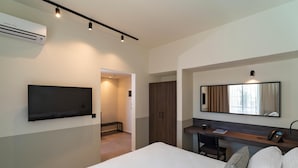 A hotel room with a bed, a desk, a chair, a TV mounted on the wall, a wardrobe, and a mirror. - Mariette Rhodes Urban Suites  (Rhodes)