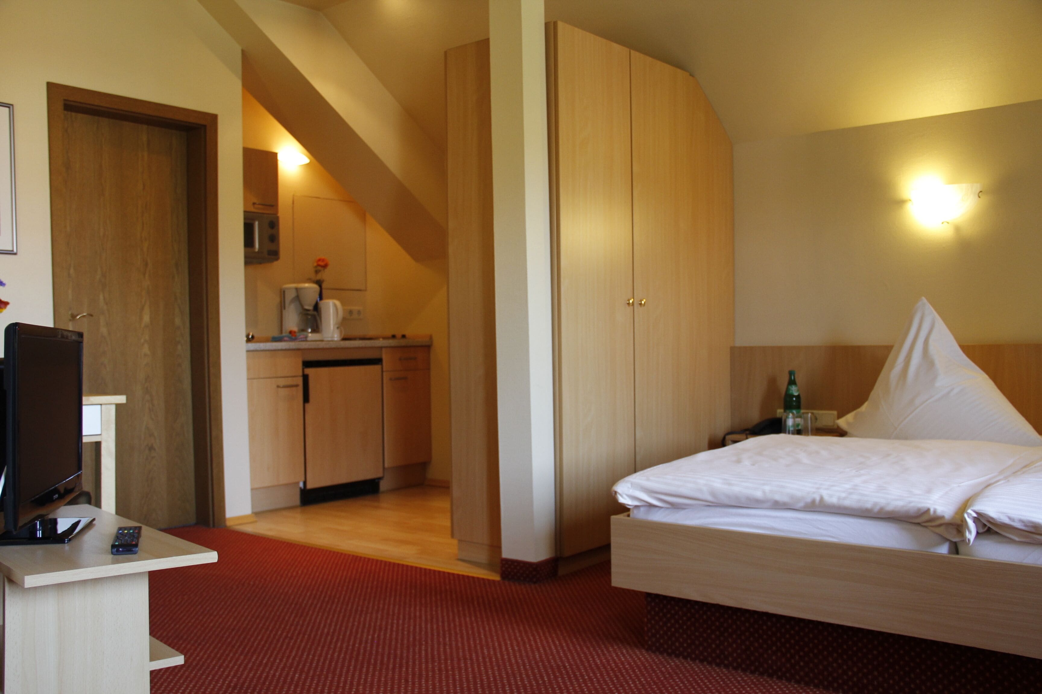 Une chambre d’hôtel comprenant un lit, un bureau avec un ordinateur et une télécommande, une kitchenette et une salle de bain.