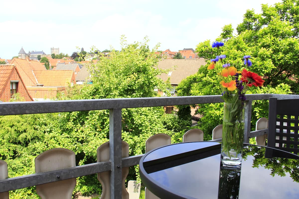 A balcony with a table and chairs, overlooking a town with houses and greenery.