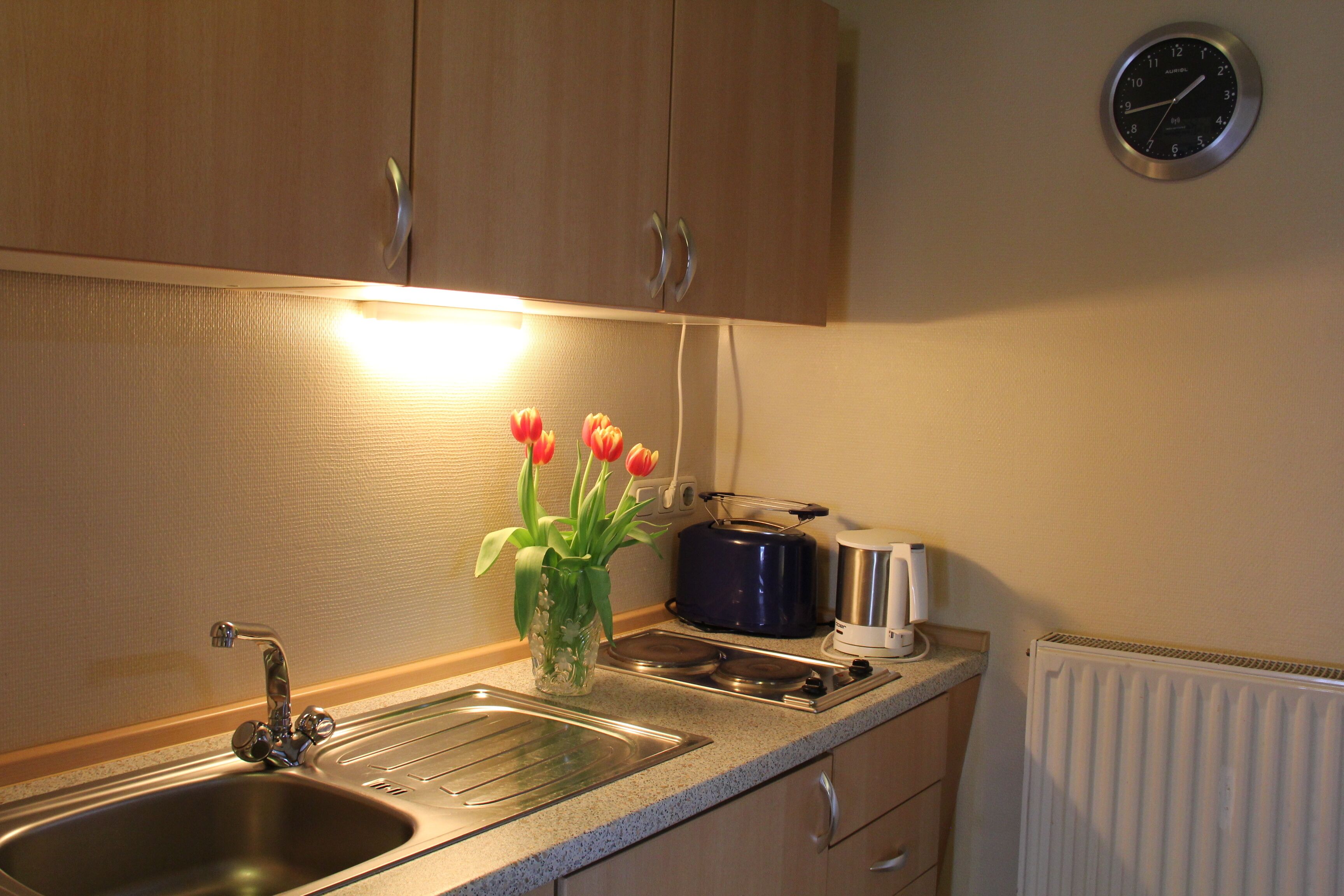 A kitchen with wooden cabinets, a stainless steel sink, a toaster, and a clock on the wall.