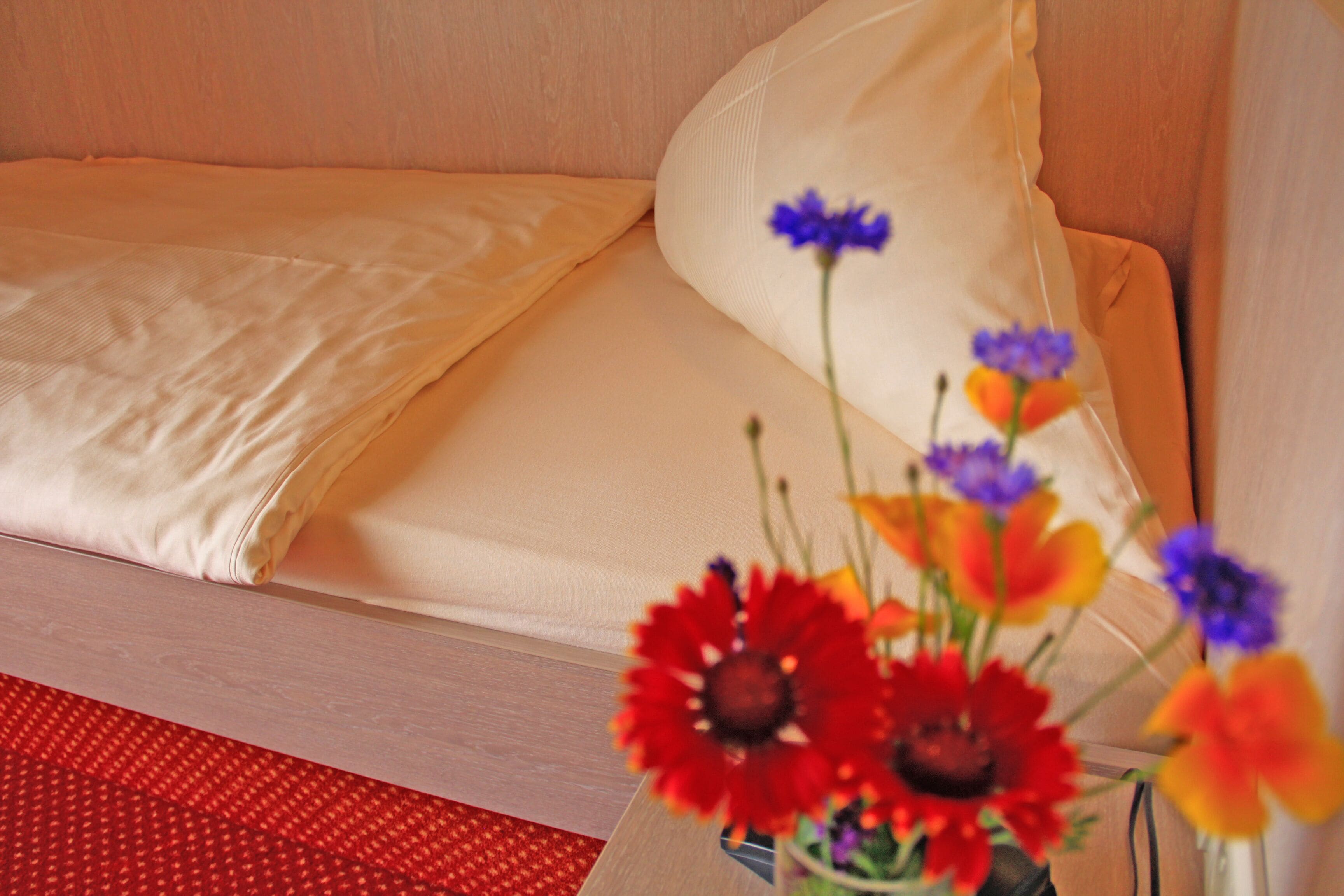 A bed with a white sheet and a red patterned rug.