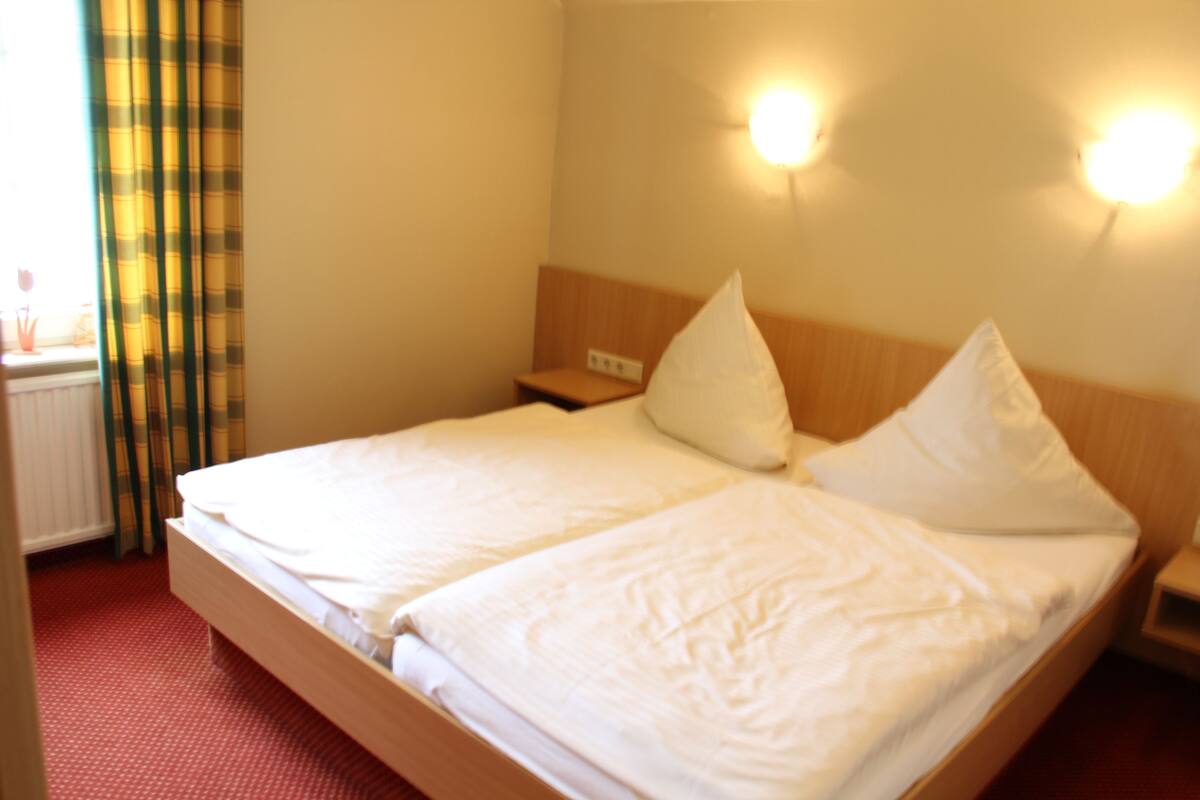A double bed with white linens, a wooden headboard, two bedside tables, and a wall-mounted light fixture.