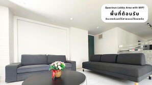 A spacious lobby area with a grey sofa, a round black table, and a vase of flowers. - The Avail (Ayutthaya)