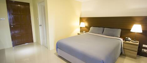 Habitación de hotel con una cama grande, lámparas de noche, cabecera de madera y mesita de noche con teléfono y lámpara.