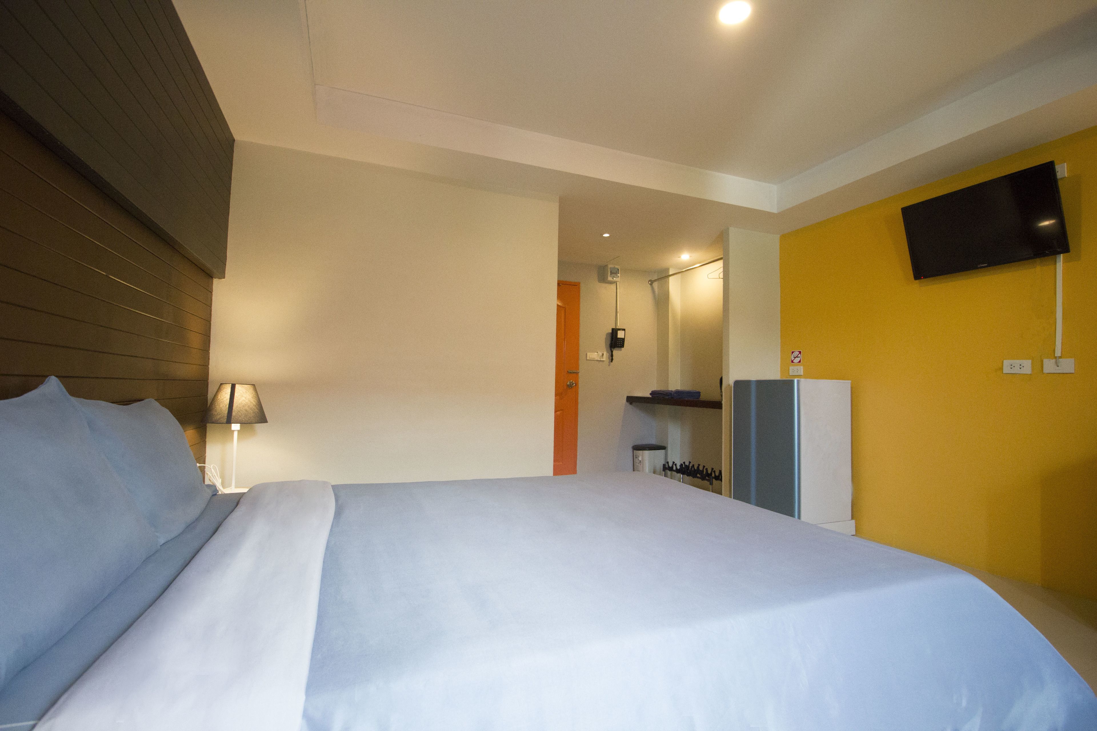A hotel room with a bed, a TV mounted on the wall, a desk, and a lamp.