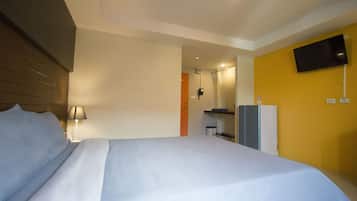 A hotel room with a bed, a TV mounted on the wall, a desk, and a lamp.
