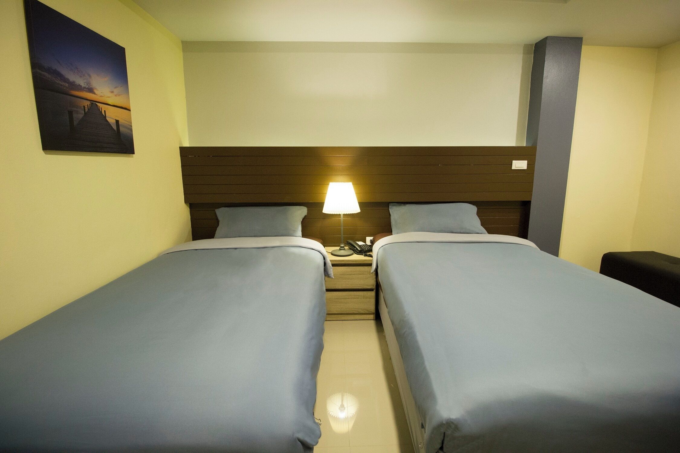 Una habitación de hotel con dos camas individuales, una mesita de noche con lámpara y un cuadro en la pared.