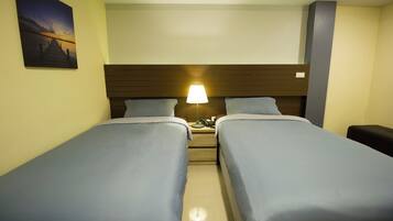 Una habitación de hotel con dos camas individuales, una mesita de noche con lámpara y un cuadro en la pared.