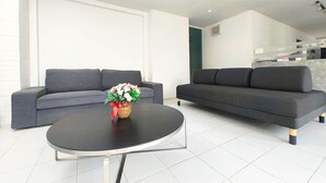 A spacious lobby area with a grey sofa, a round black table, and a vase of flowers. - The Avail (Ayutthaya)