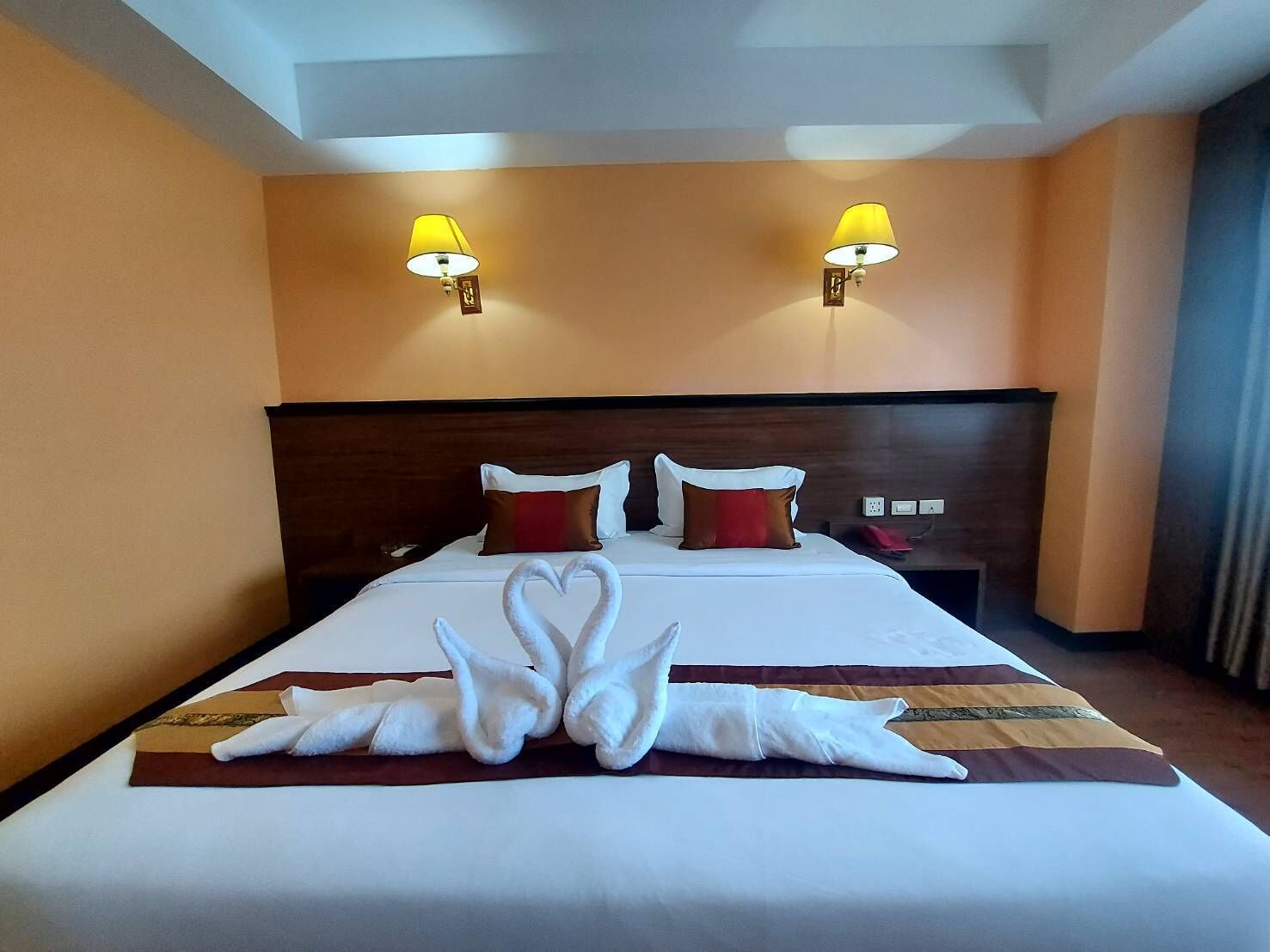A hotel room with a large bed, two bedside lamps, and a heart-shaped towel arrangement on the bed.