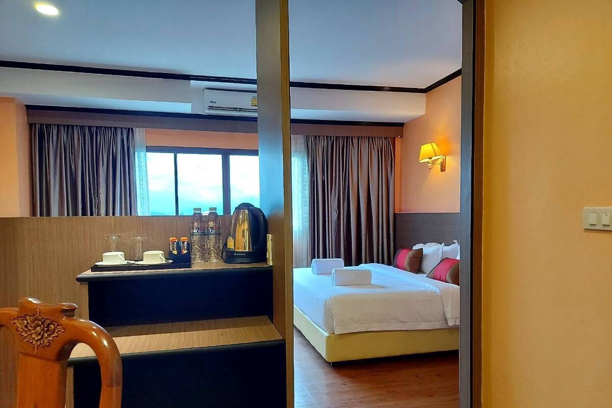 A hotel room with a bed, a desk with a coffee maker, and a view of the outdoors through the window.
