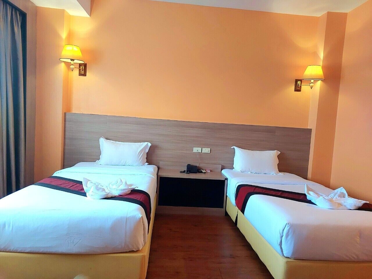 Ein Hotelzimmer mit zwei Einzelbetten, einem Holzkopfteil, Nachttischlampen und einem kleinen Tisch zwischen den Betten.