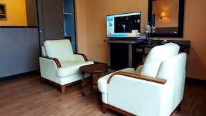A hotel room with two white leather armchairs, a small wooden table, a television, and a mirror on the wall. - M Hotel Danok (Sadao)