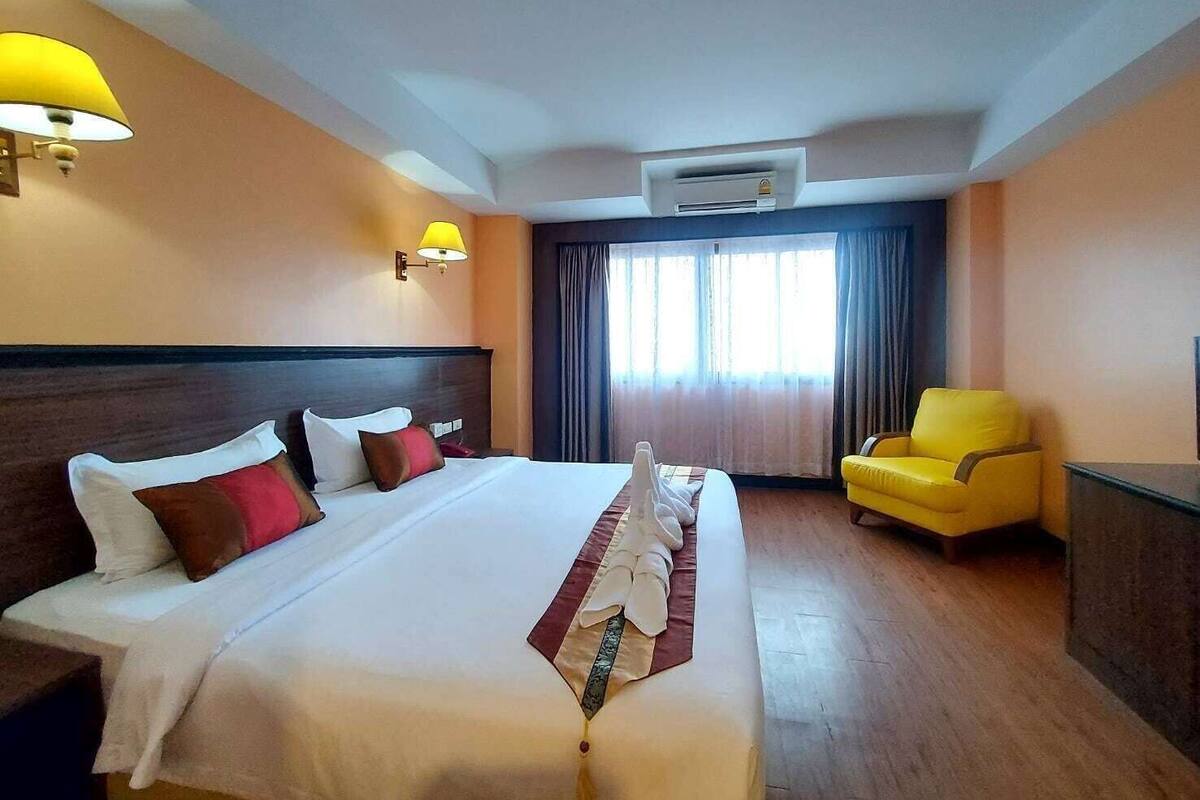 Ein Hotelzimmer mit einem großen Bett, einem Sessel, einem Schreibtisch und einem Fenster mit Vorhängen.