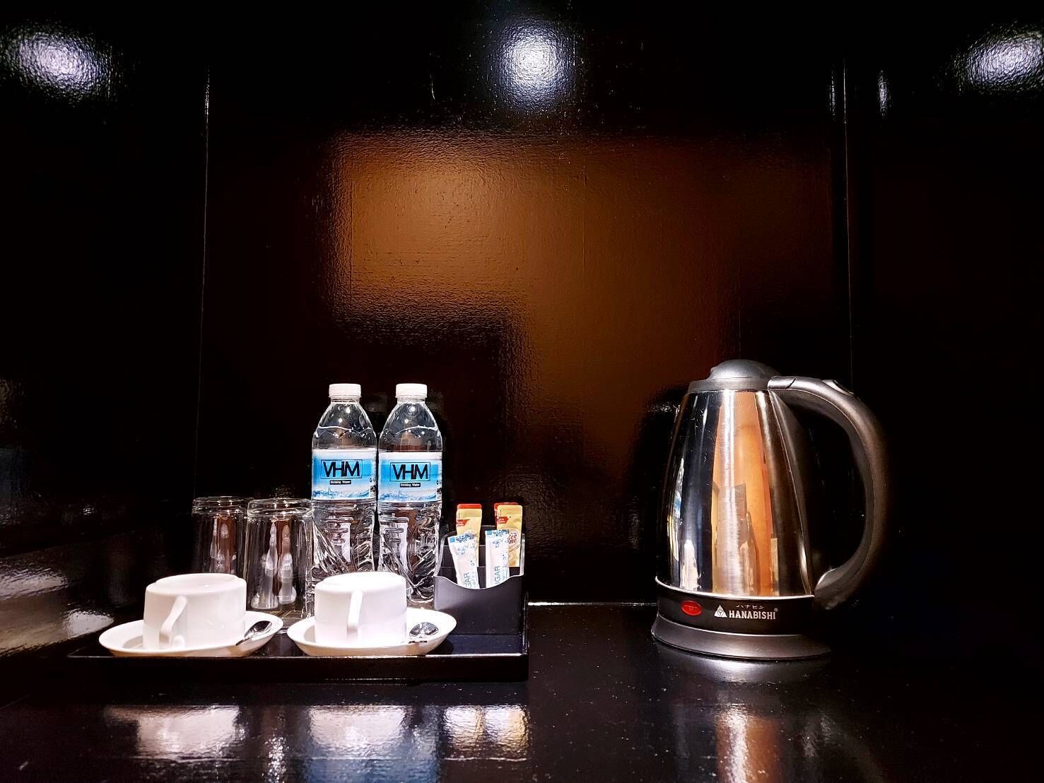 Un espai per fer cafè amb una cafetera d'acer inoxidable, dues ampolles d'aigua i una safata amb tasses i platets.