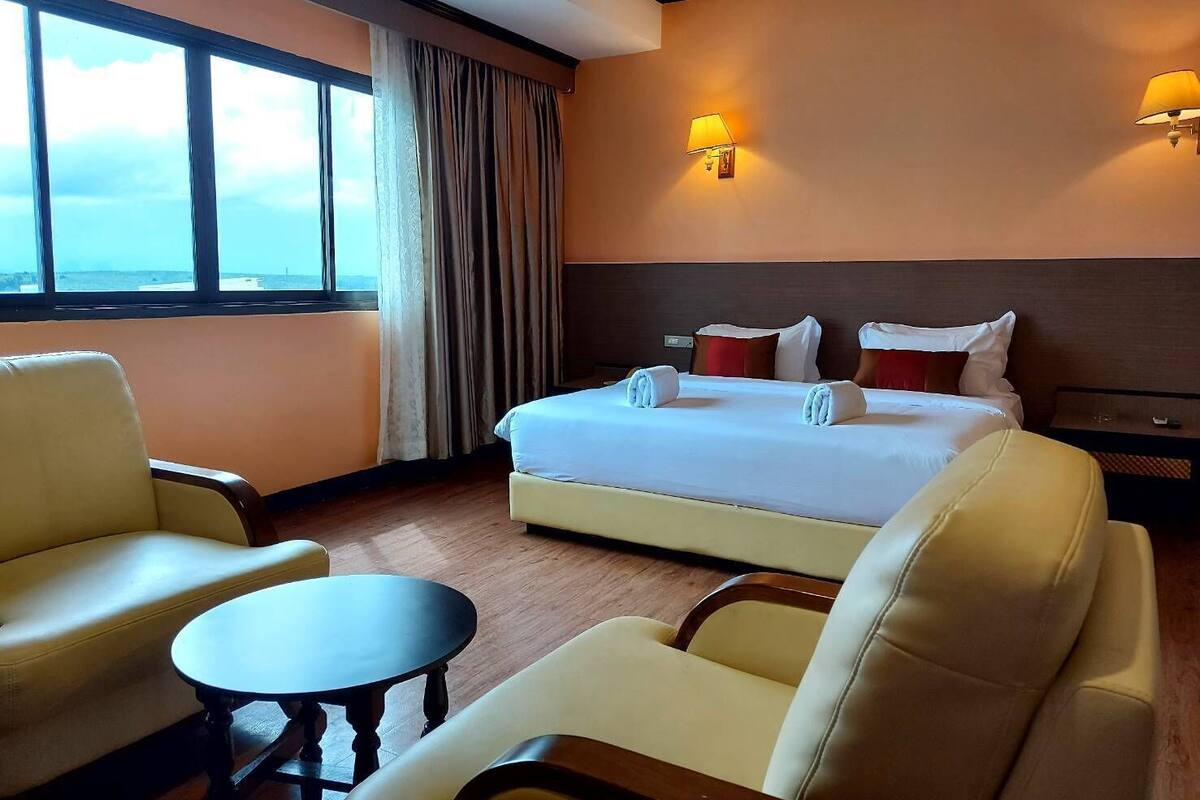 A hotel room with a bed, two armchairs, a small table, and a window with curtains.