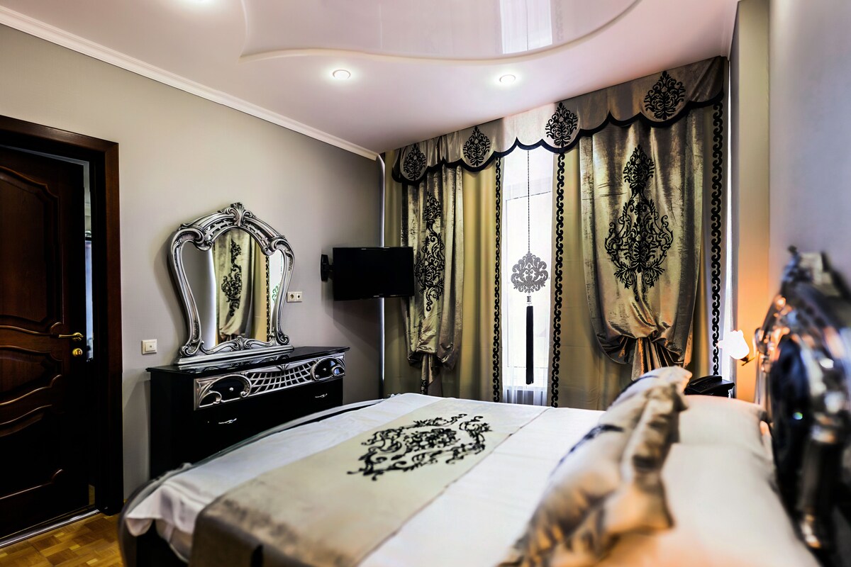 A bedroom with a bed, a dresser, a mirror, a television, and curtains.