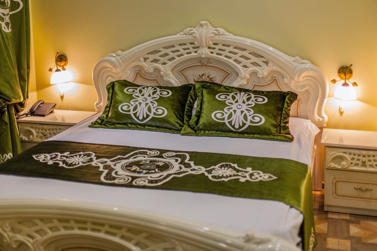 A bed with a white headboard, green pillows, and a decorative bedspread. There are two bedside tables with lamps and a telephone on one.