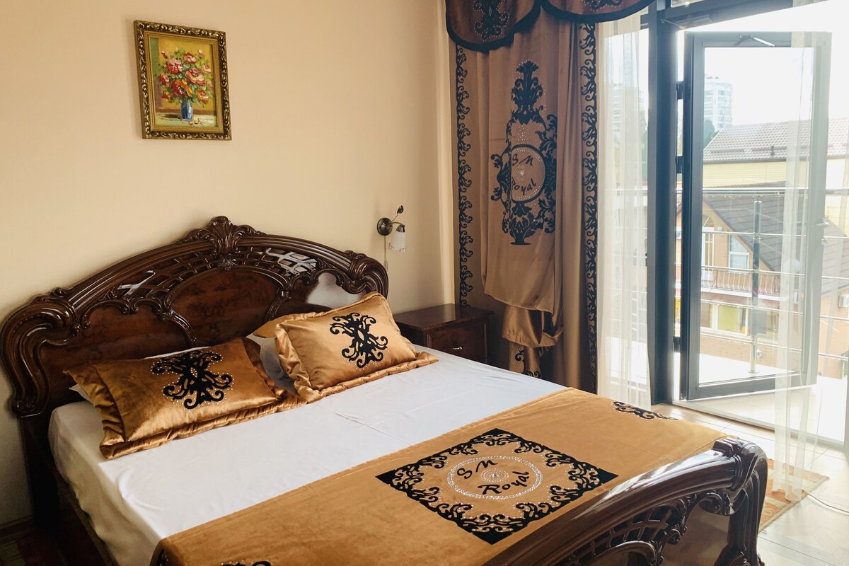 A bed with a brown bedspread and matching pillows, a wooden headboard, a framed picture on the wall, and a view of the outside through a glass door.