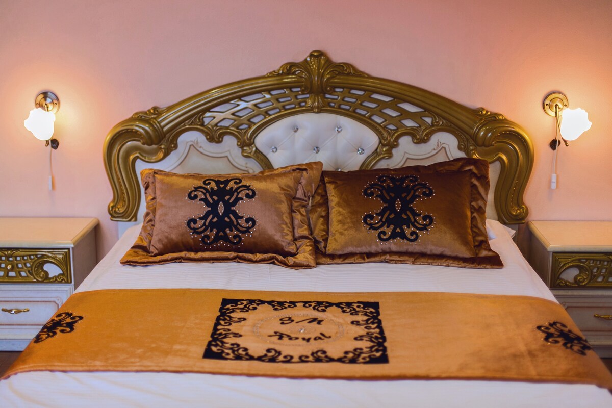 A bed with a gold headboard, two decorative pillows, and a gold throw blanket.